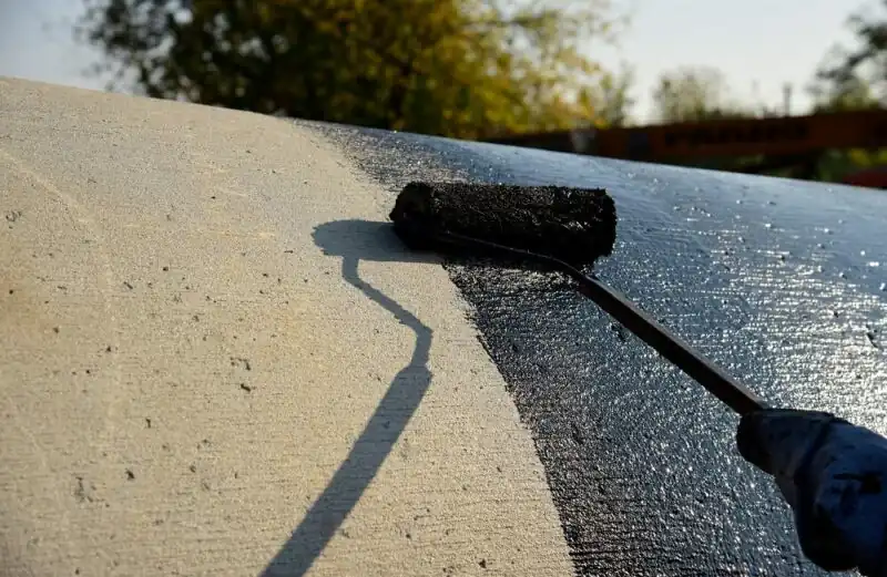 Bitumina farbo aplikata per rulpremilo sur betonsurfaco por akvorezisto kaj korodprotekto.
